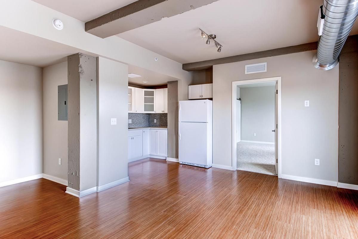 Empty apartment with hardwood floors, kitchen, and open doorway, neutral colors.