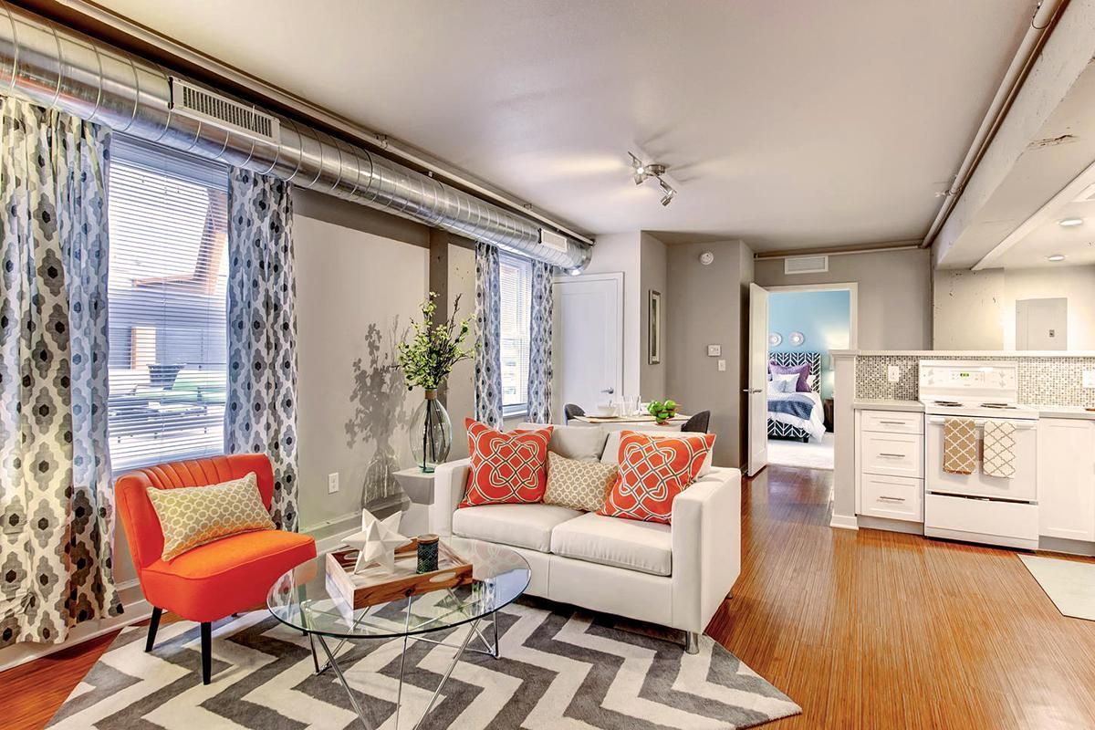 Living room with white sofa, orange chair, patterned curtains, and open kitchen.