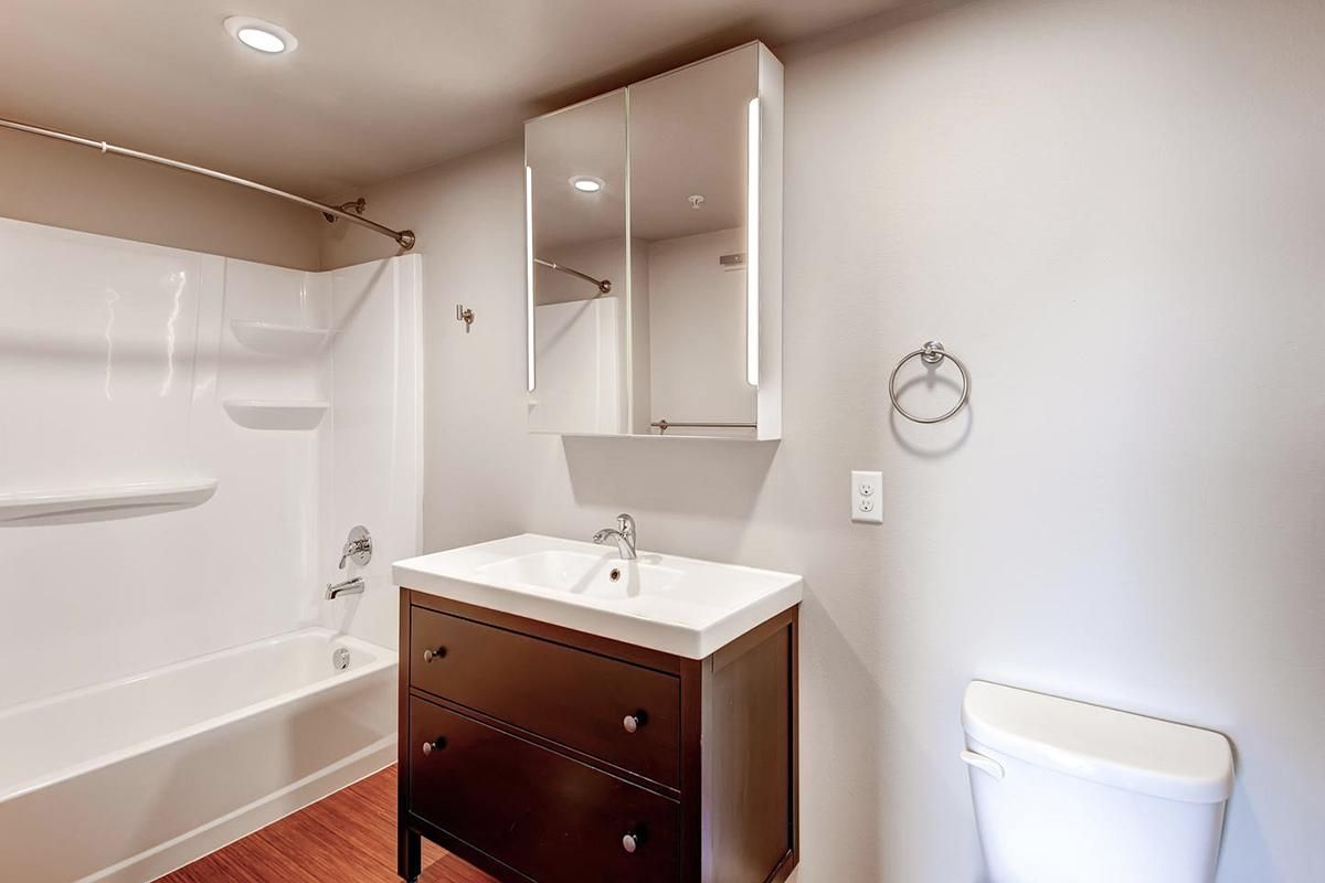 Bathroom with dark brown vanity, white sink and toilet, and white bathtub.