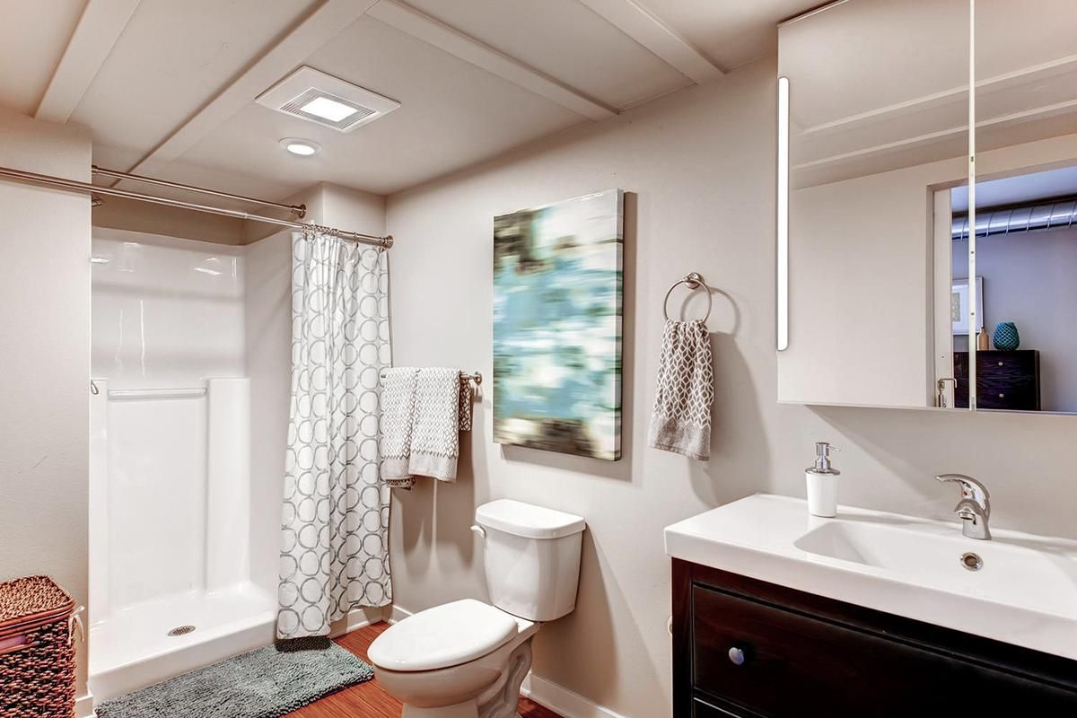 Bathroom with white shower, toilet, sink, dark cabinet, light walls, and art.