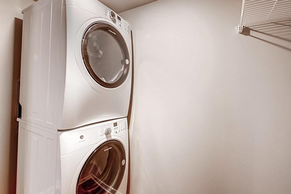 Stacked white washer and dryer in a laundry room, with a metal shelf to the right.