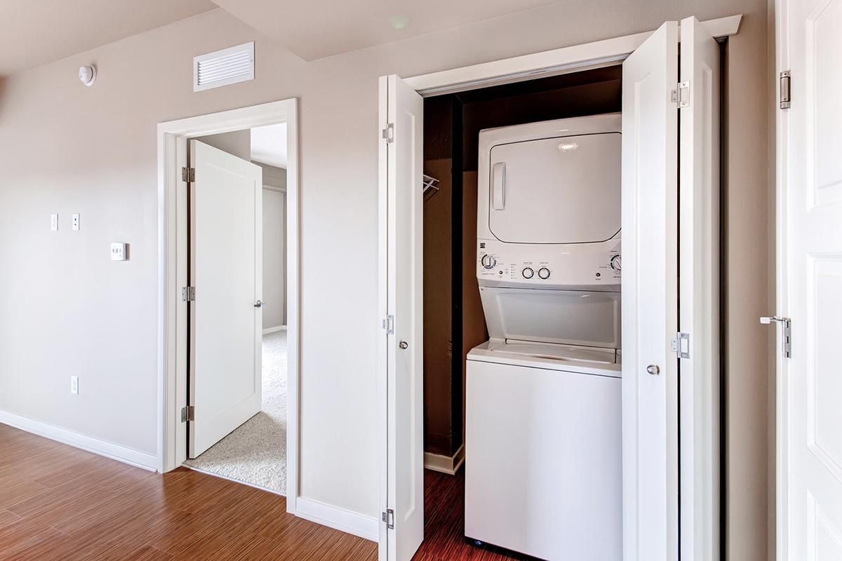 Laundry room with stacked white washer and dryer behind folding doors, doorway on left.