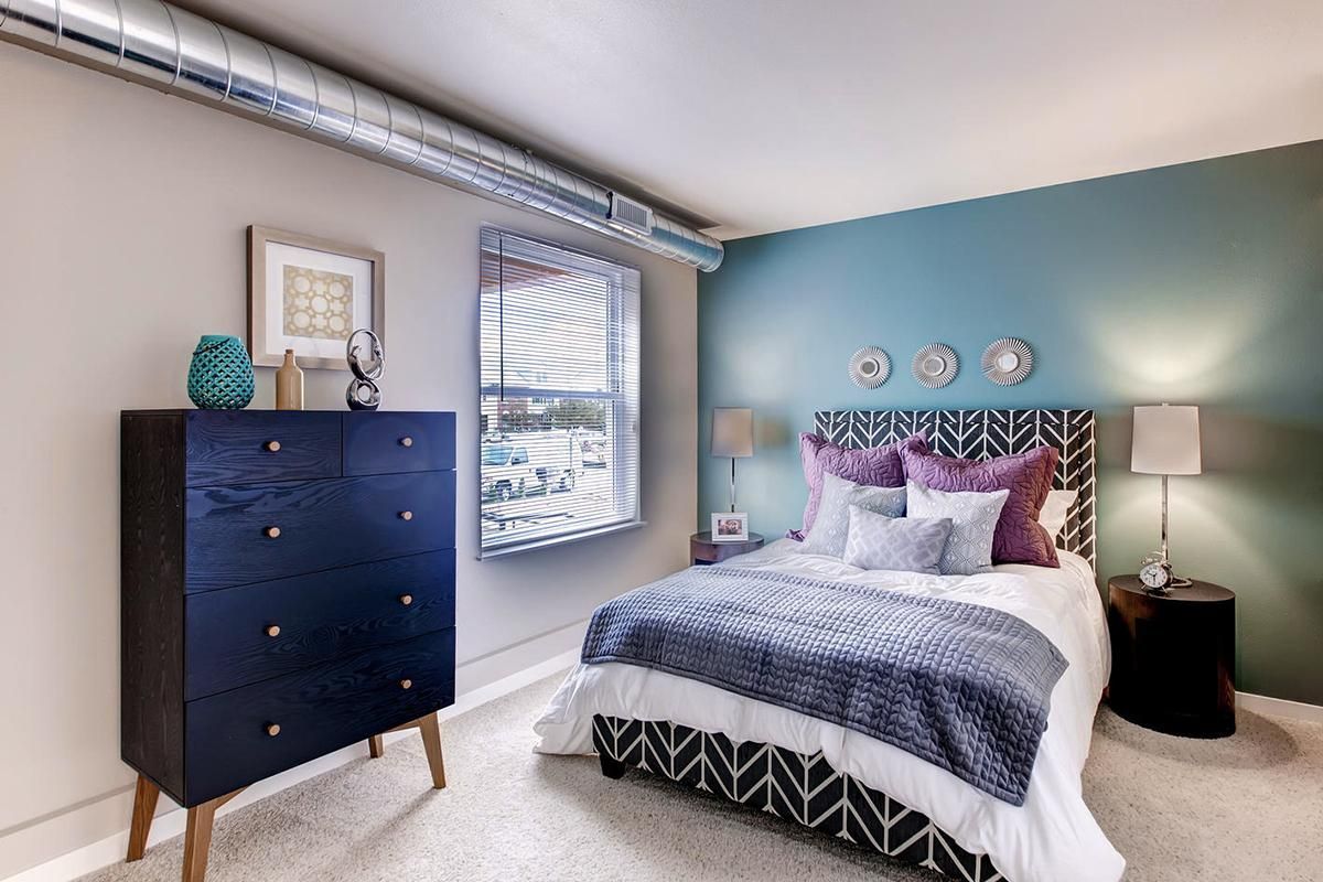 Bedroom with bed, dark blue dresser, teal accent wall, and patterned bedding.