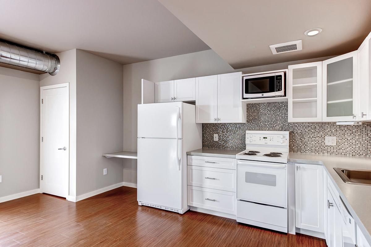 White kitchen with appliances, cabinets, and a microwave.  Wood floor and a small desk.