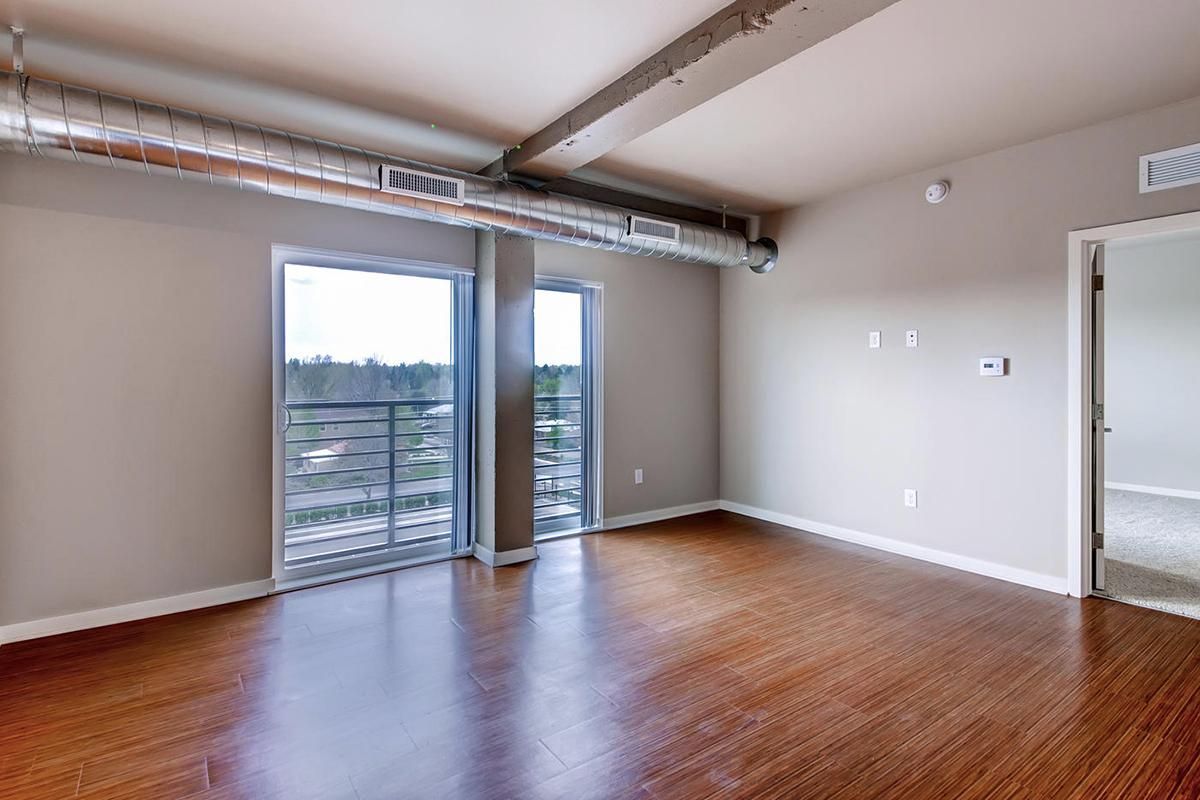 Empty modern apartment with wood floors, large windows, and exposed ductwork.