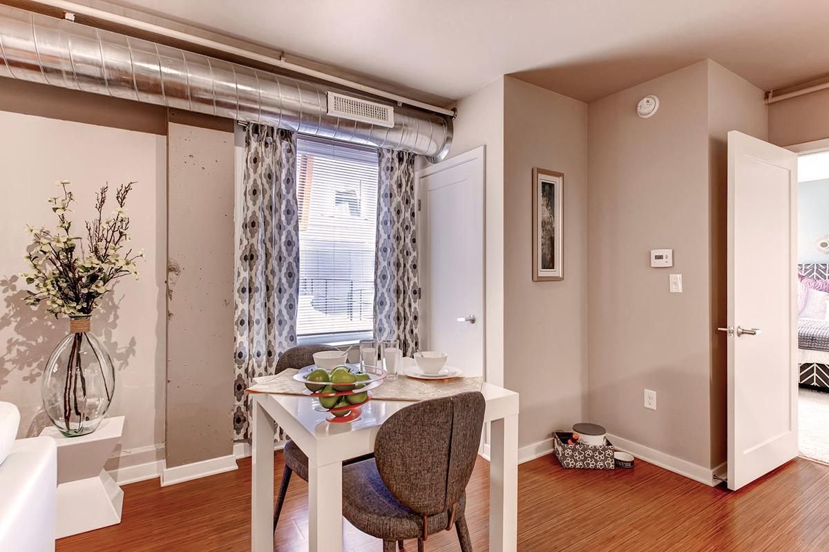 Dining area with table set for meal, window with curtains, and vase of flowers.