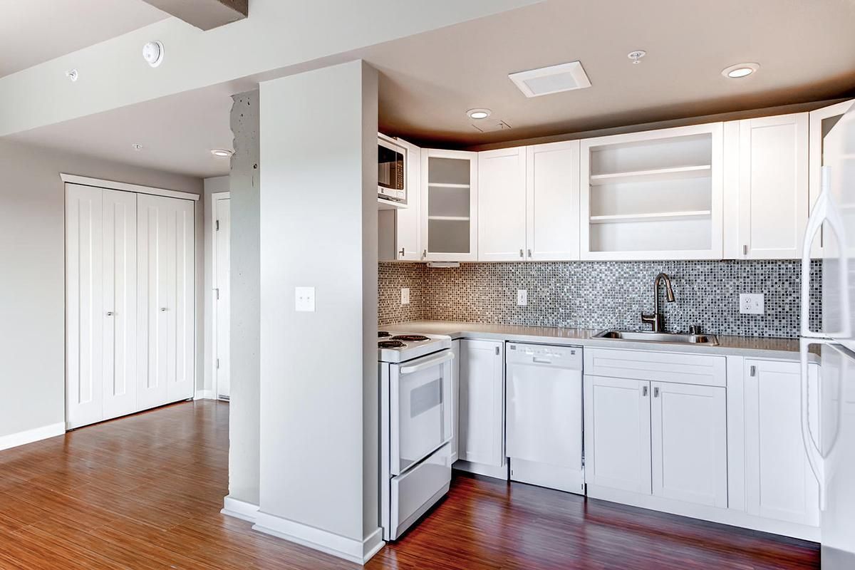 Kitchen with white cabinets, stove, and patterned backsplash; hardwood floors and closet in the background.
