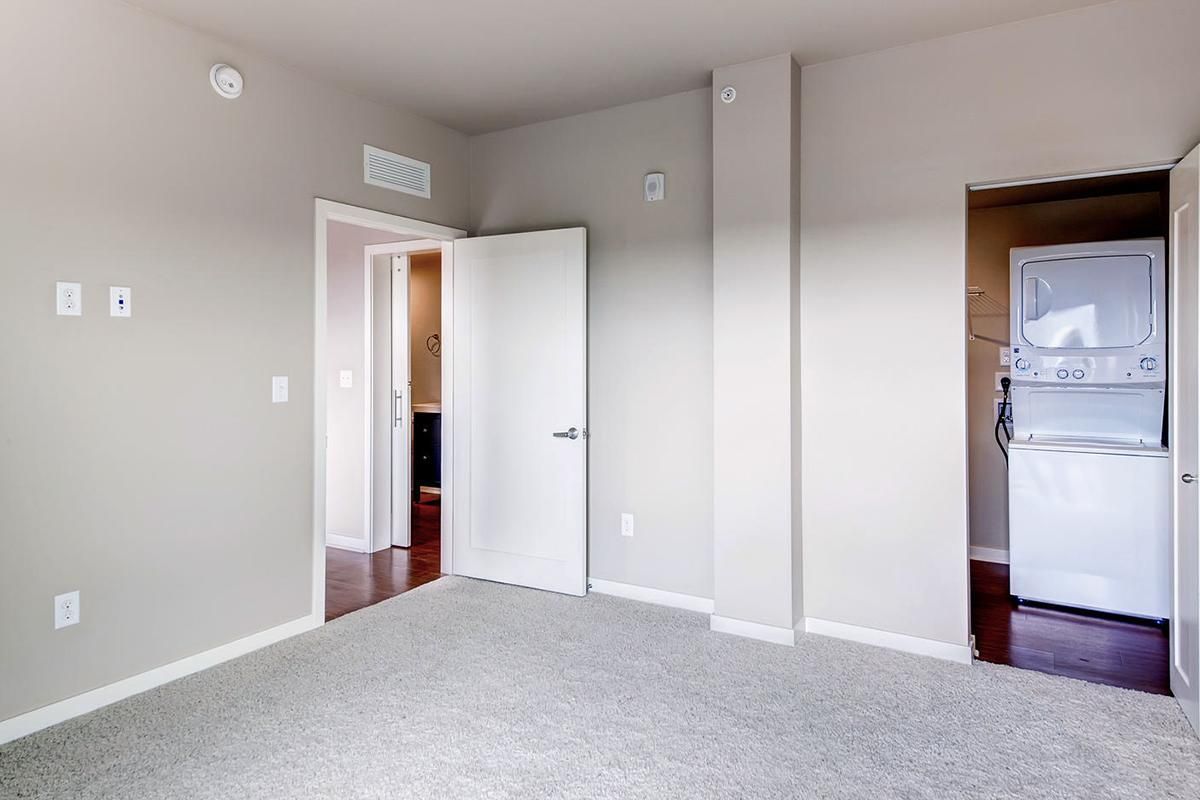Empty bedroom with carpet, doors, and a stacked washer/dryer in a closet.