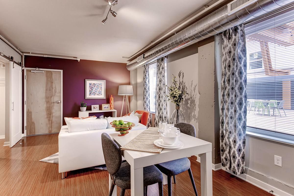 Dining area with table, chairs, sofa, curtains, and wooden floor. Purple wall, white accents.