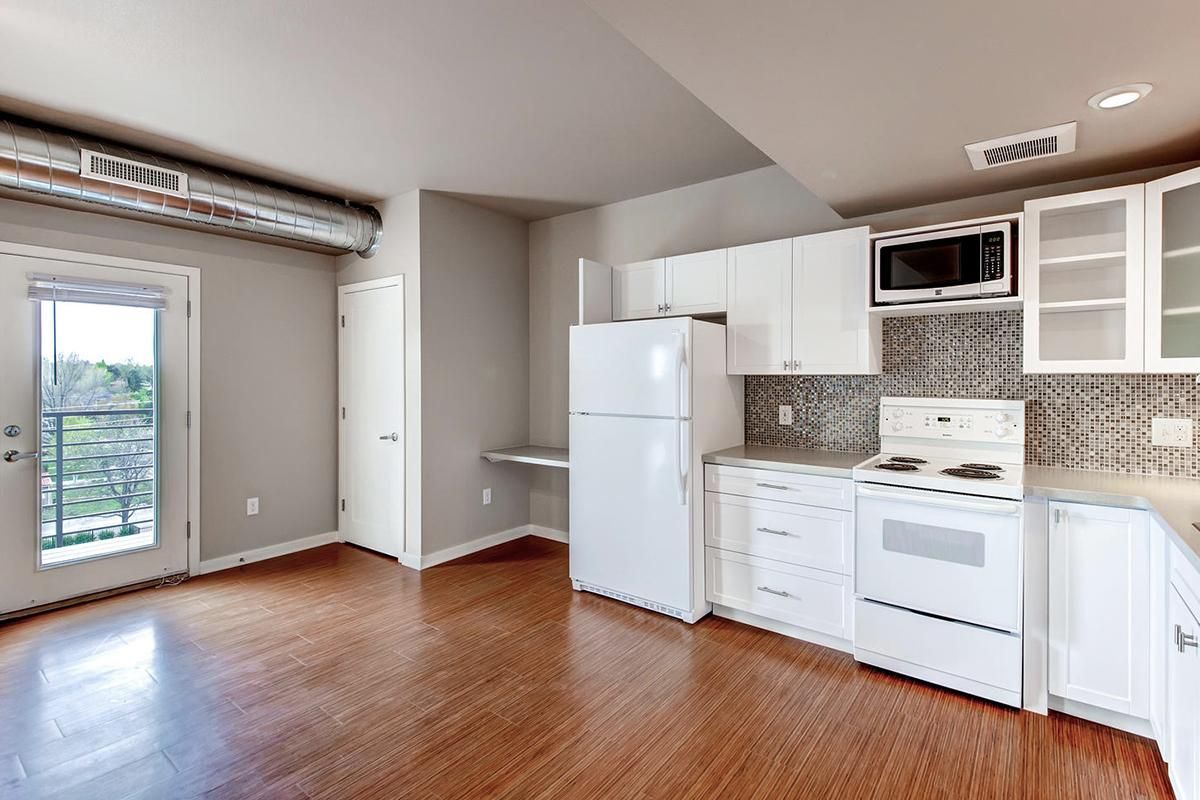 Interior of a kitchen with white appliances, wooden floor, and a door leading to a balcony.