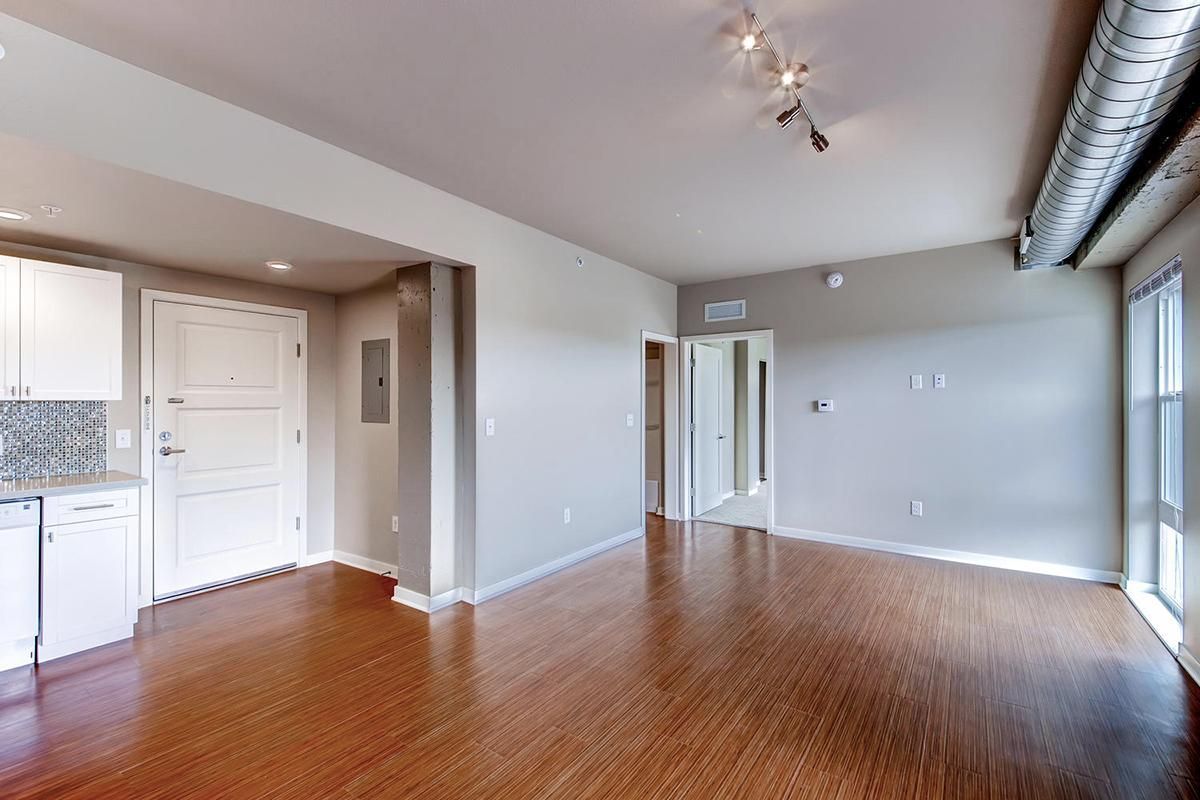 Empty modern apartment with hardwood floors, light gray walls, and white cabinets.