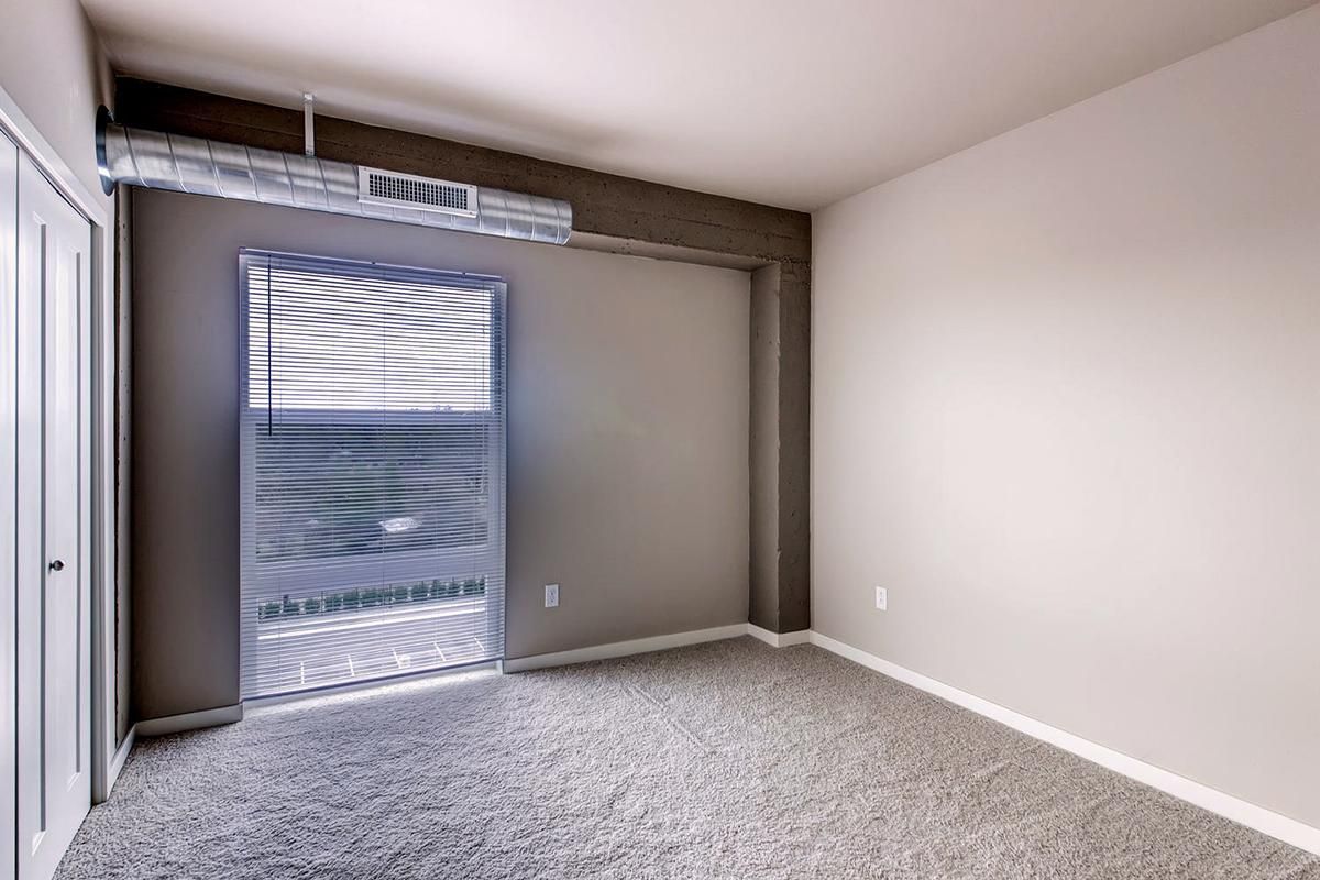 Empty room with gray carpet, a doorway with blinds, and neutral-colored walls.