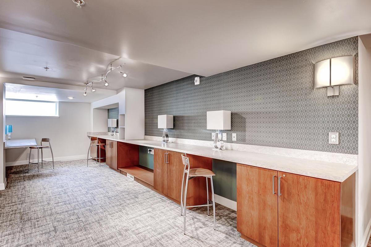 A long room with a countertop and cabinets for work. Grey tiled wall, carpeted floor, and various desk lamps.