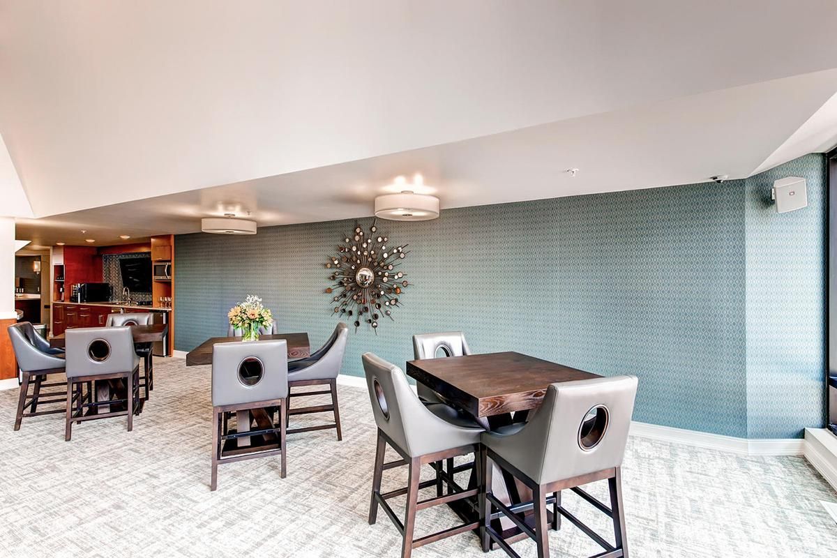 A modern lounge with tables, bar stools, patterned blue wall, and large windows.