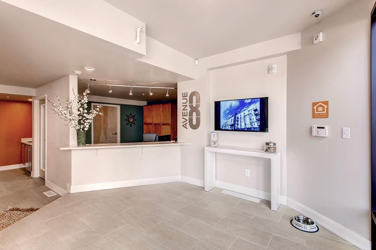 Lobby with front desk, TV, and dog bowl. Beige and orange walls, tan flooring. 