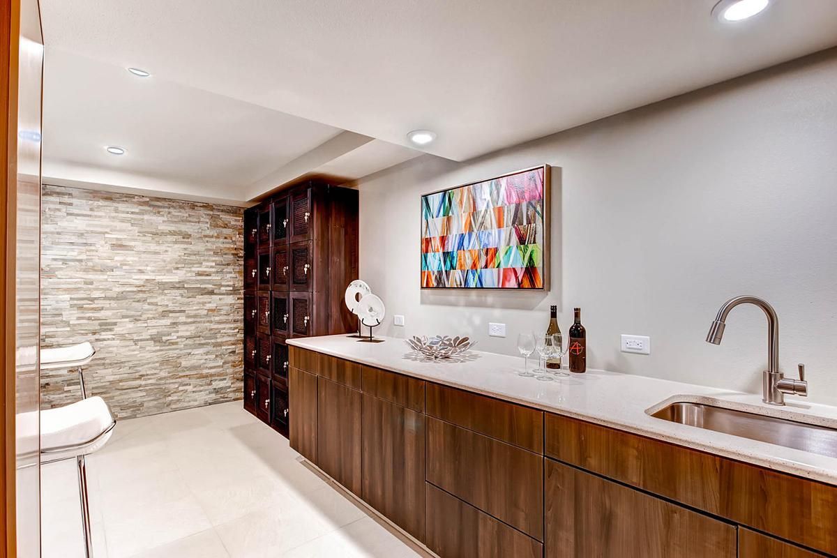 Wine cellar with stone wall, wooden cabinets, sink, and colorful artwork.