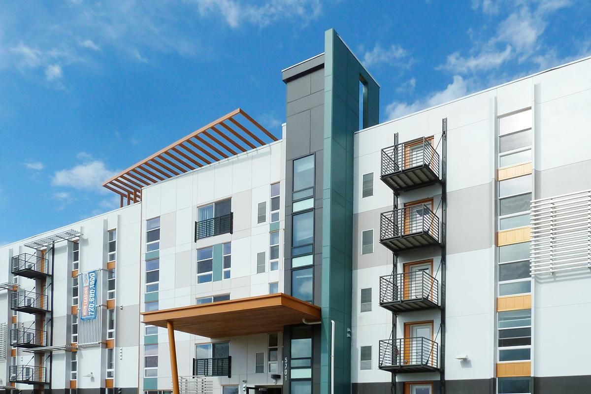Modern apartment building exterior with balconies, blue sky backdrop.