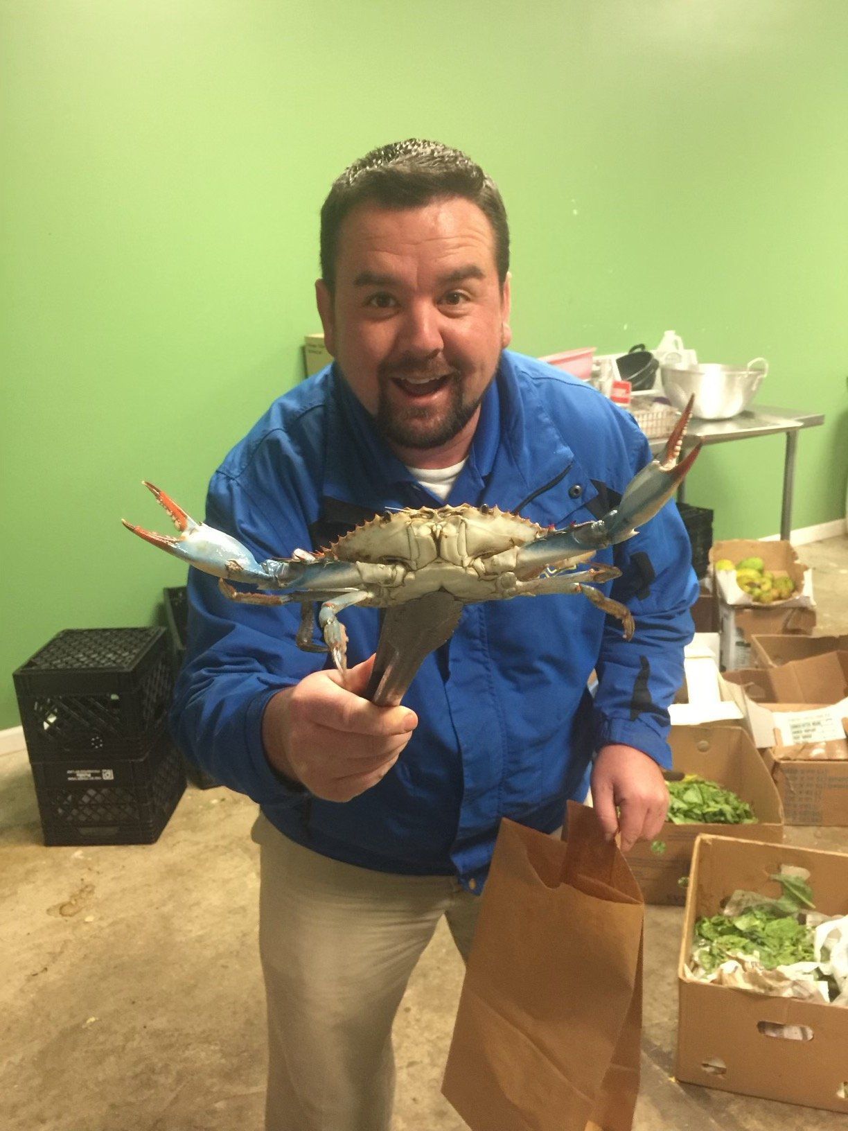 A man at Indoor Outdoor Security in a blue jacket is holding a blue crab in his hands.