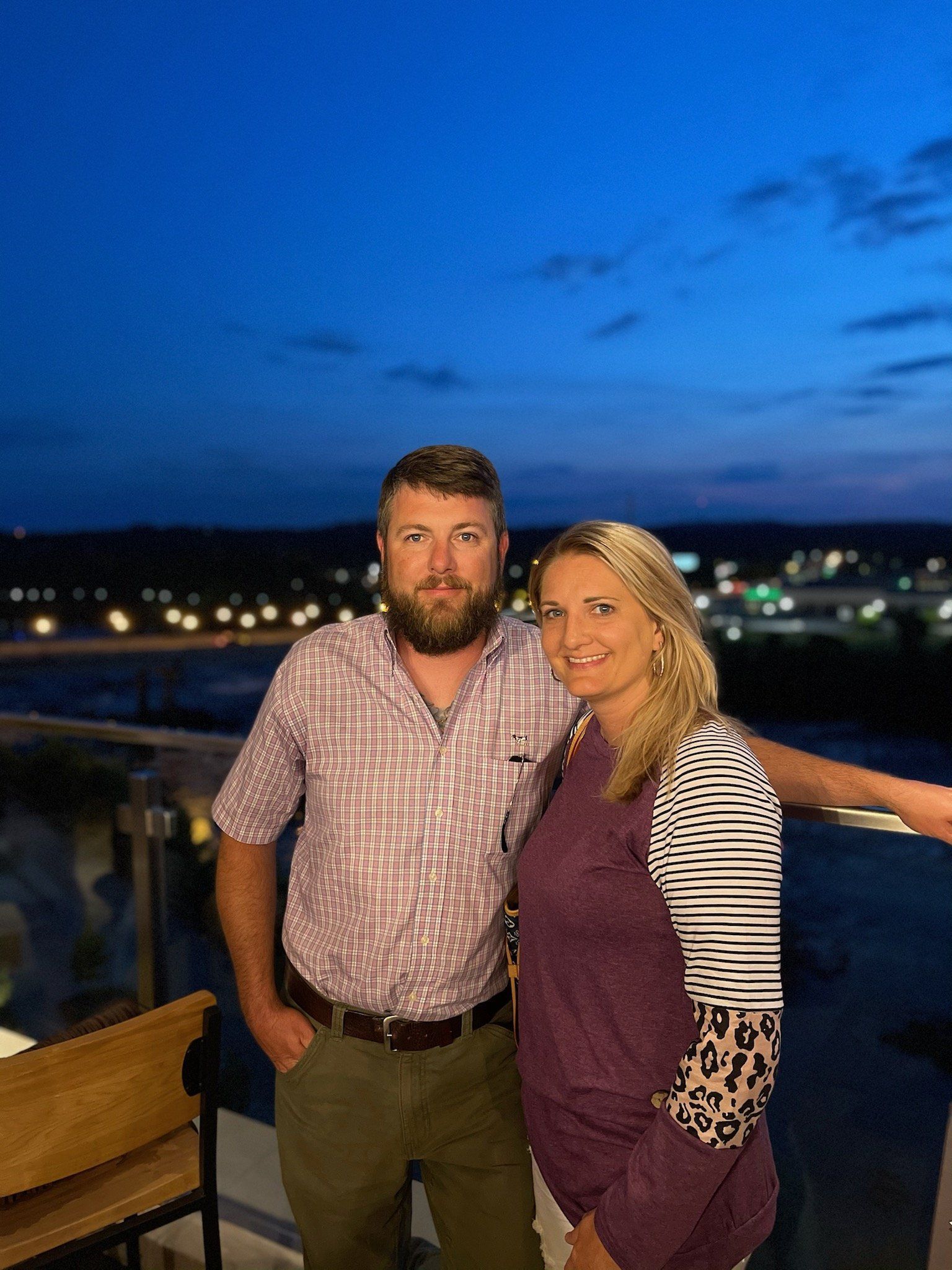 Owner of Indoor Outdoor Security and his wife are posing for a picture on a balcony at night.