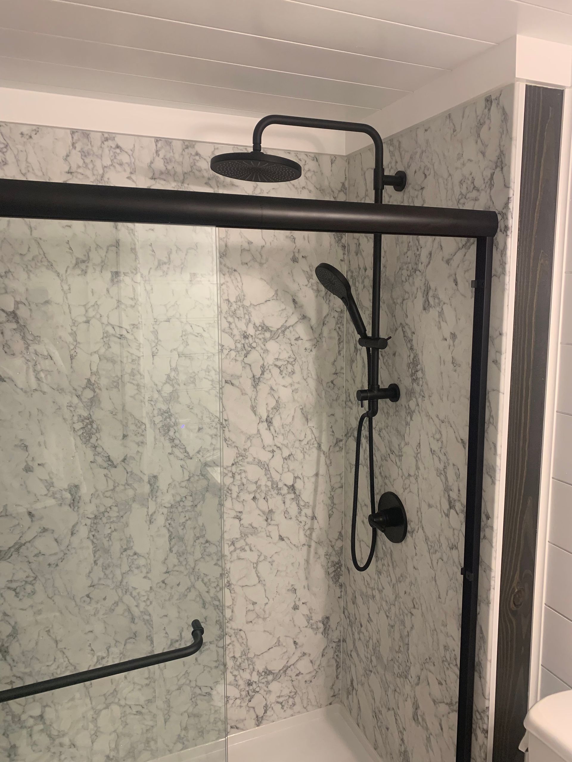 Rightway Plumbing Sewer And Drain - A bathroom with marble walls and a black shower head.