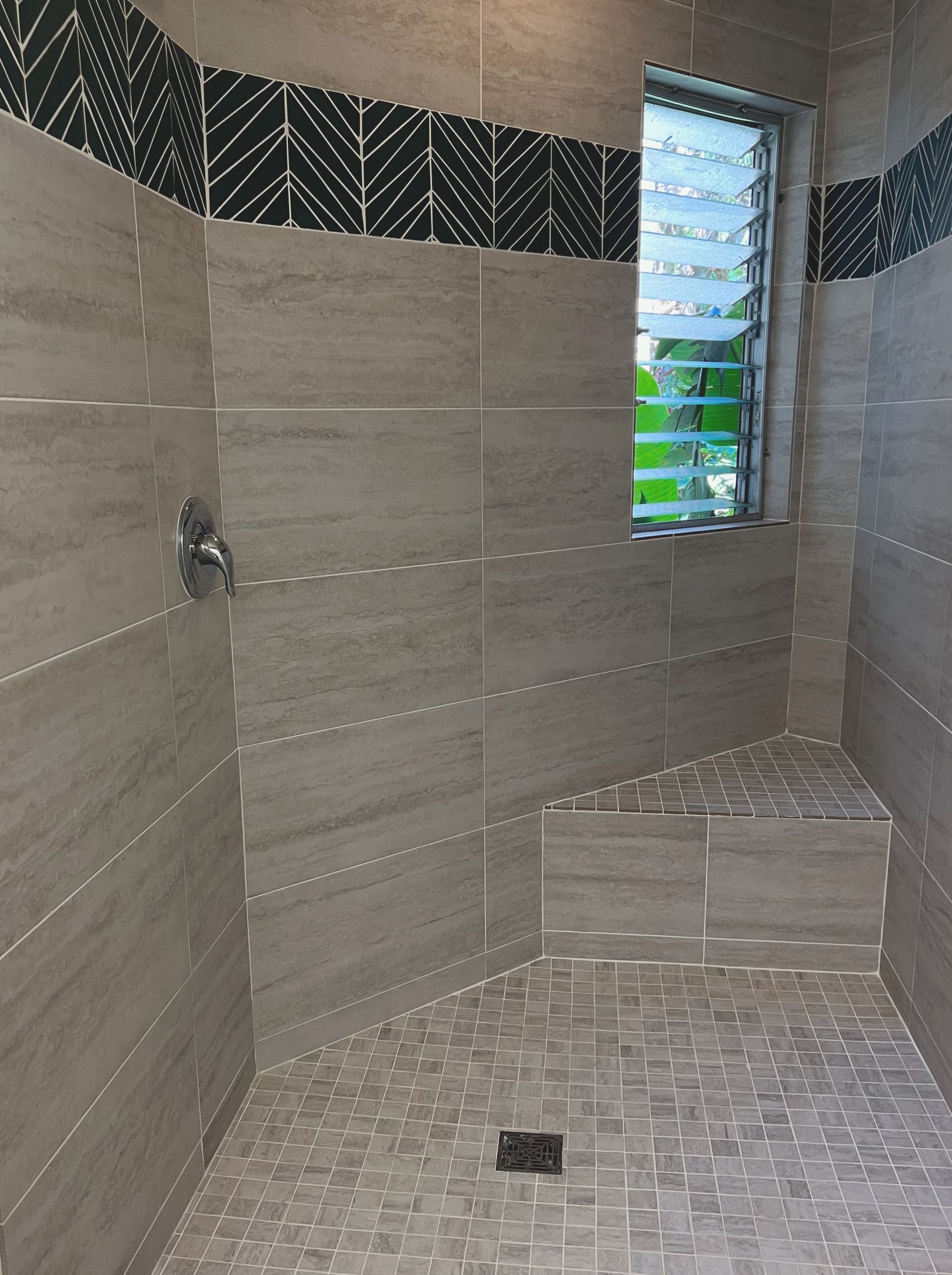 Tiled shower with beige walls, patterned trim, built-in seat, and window.