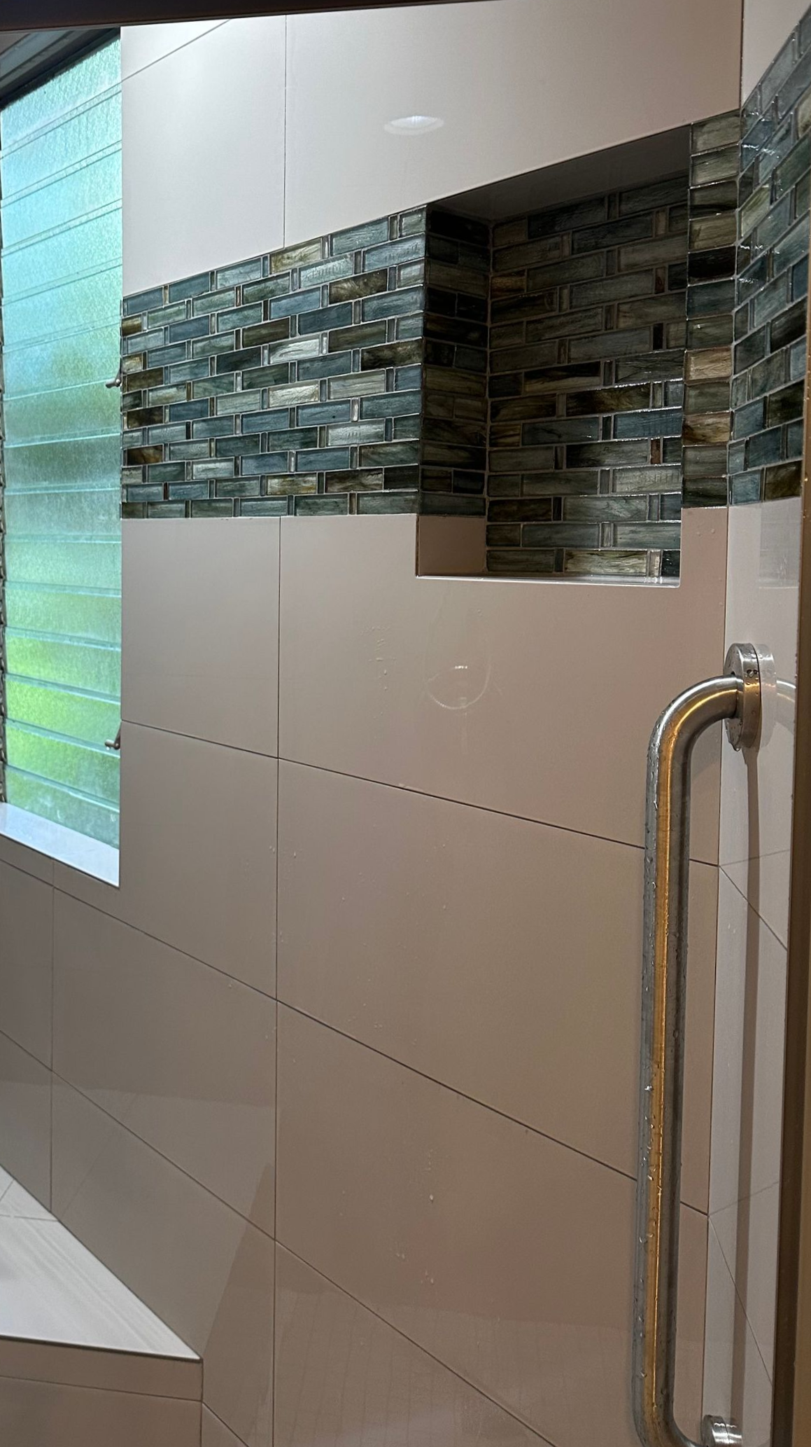 Shower interior with niche and glass tile accents; a grab bar is visible.