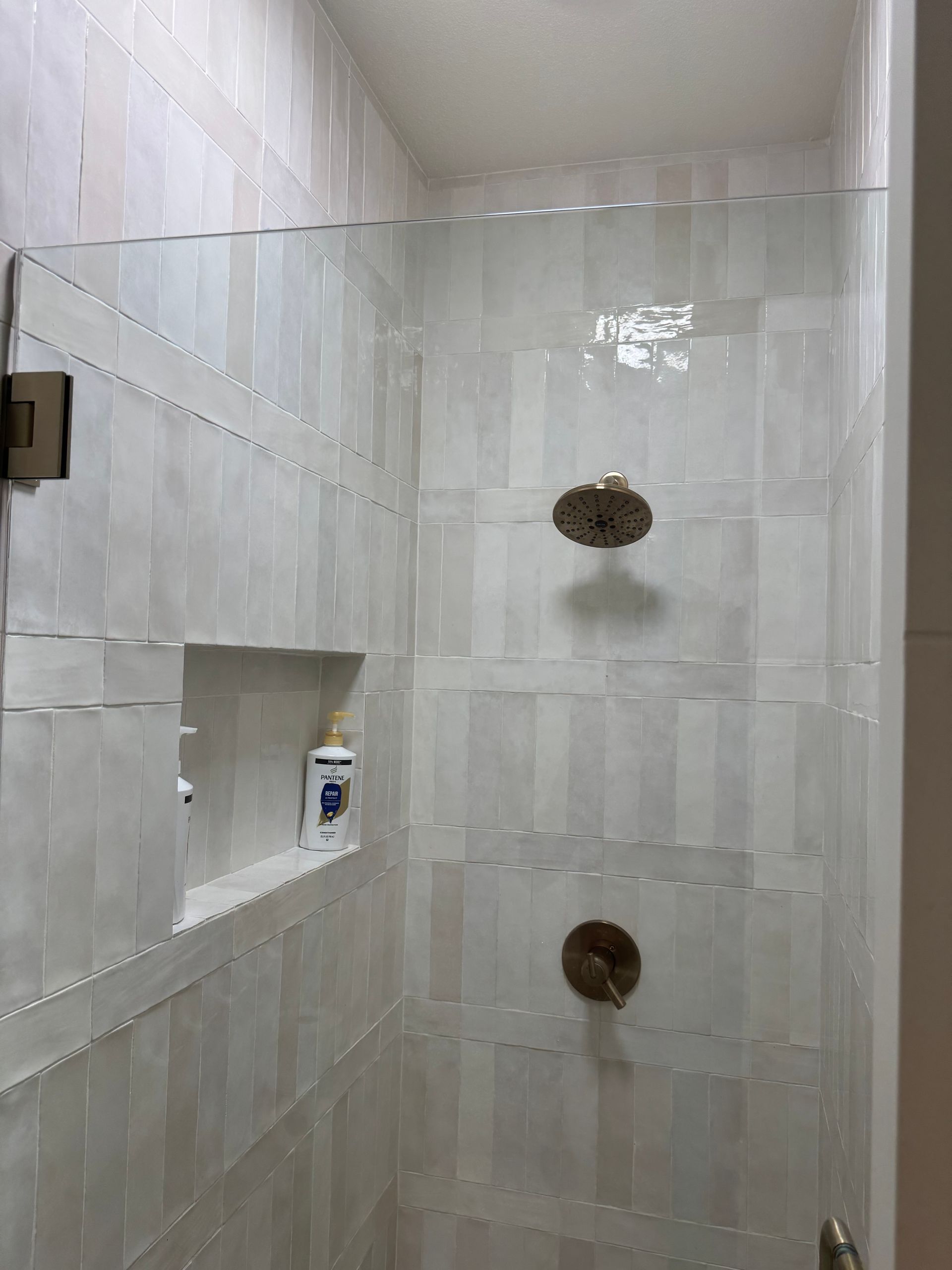 Shower with glass door, white tiled walls with niche, and brass fixtures.