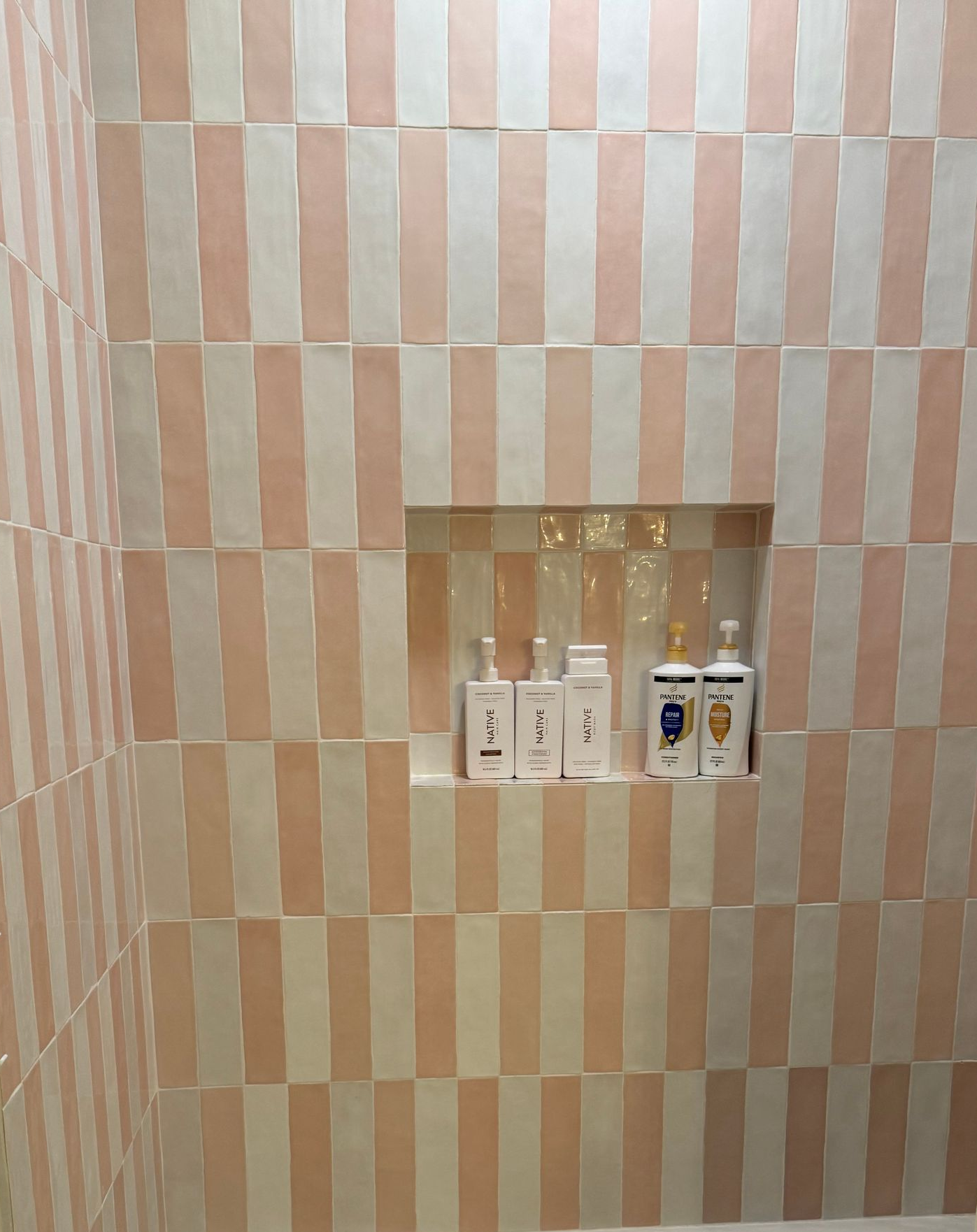 Pink and white striped tile shower wall with a niche.