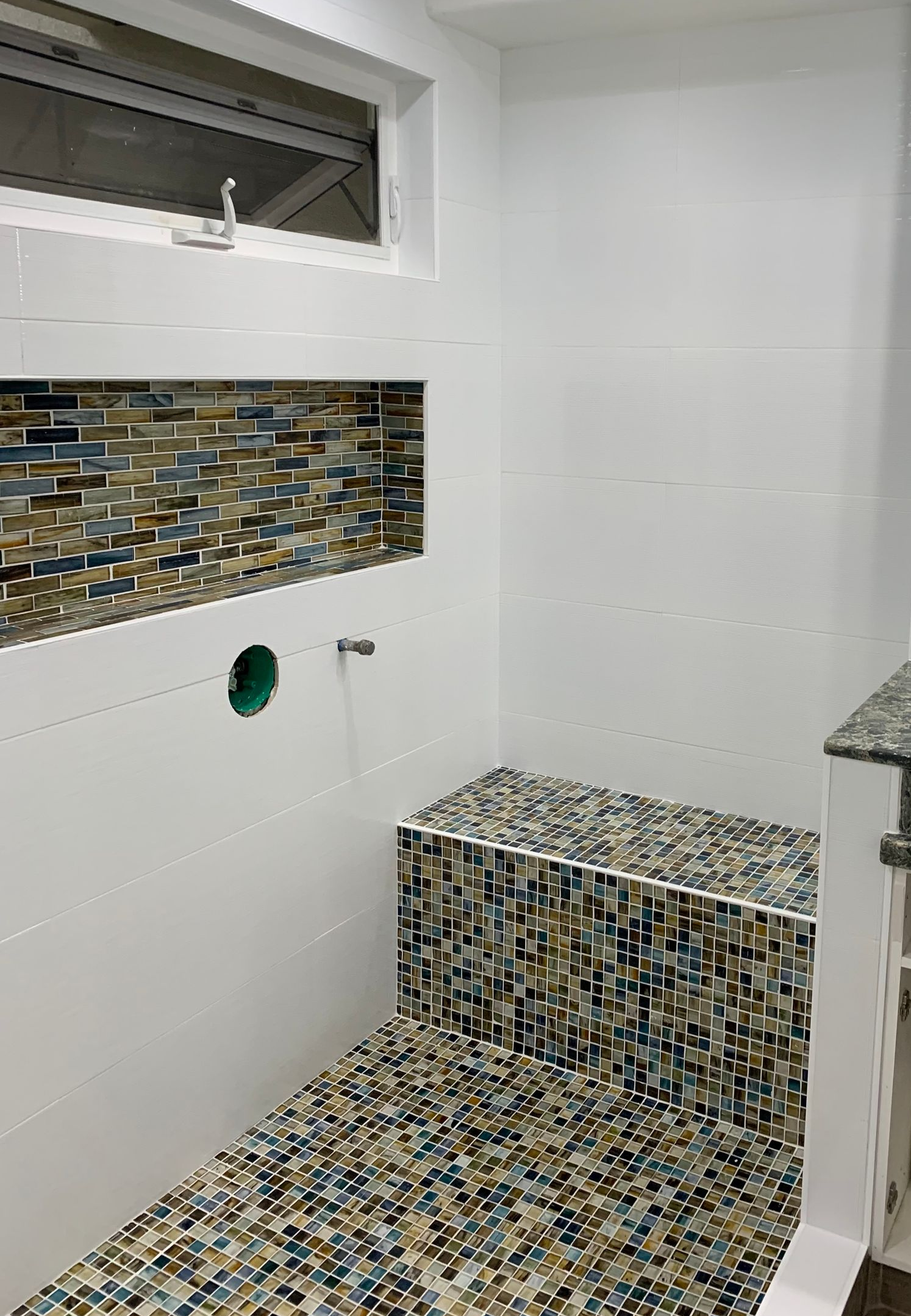 Bathroom with mosaic tile accents and white walls. Window above tile niche and built-in bench.