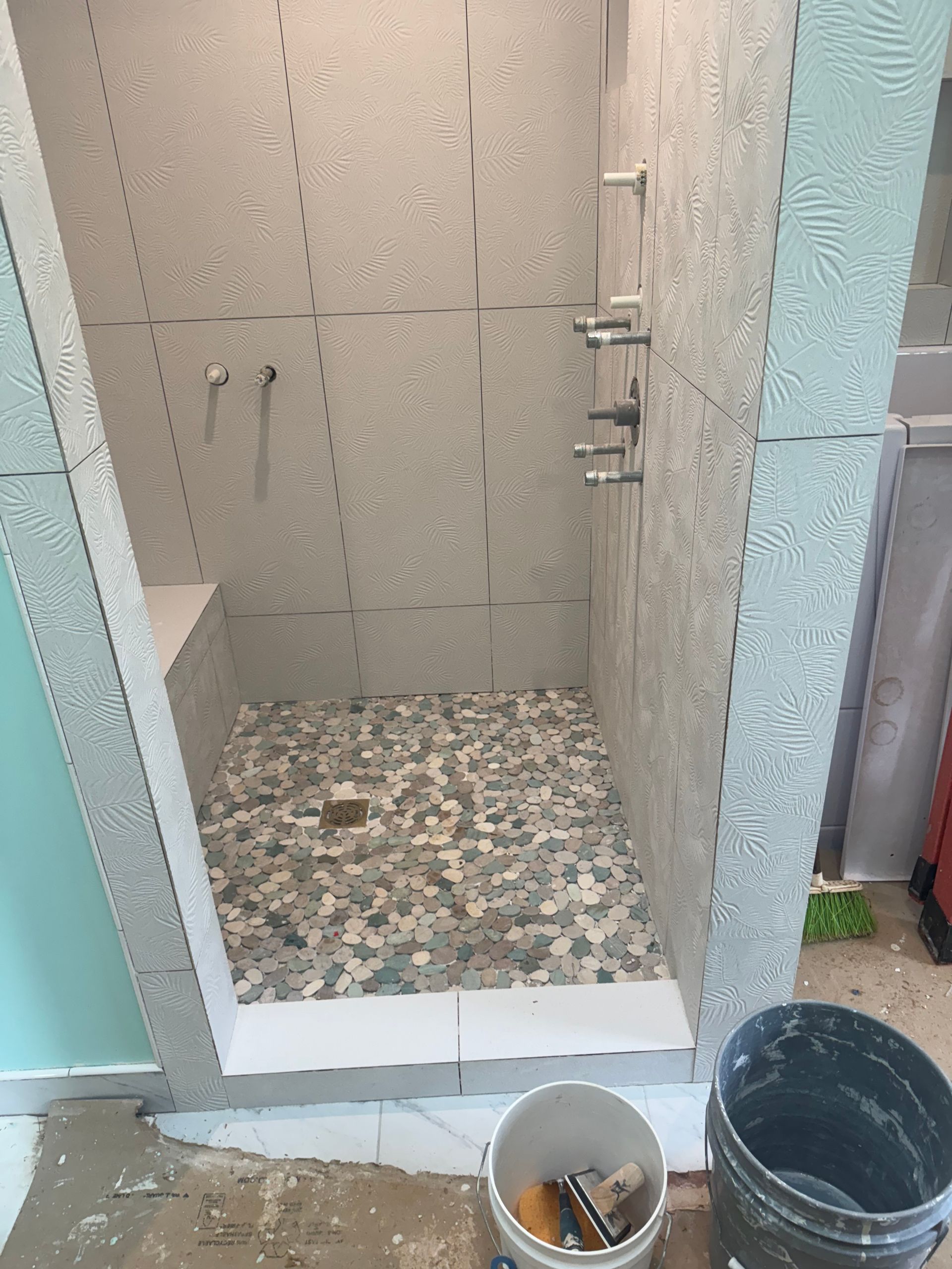 Partially constructed shower with textured gray walls and pebble floor. Features built-in bench and multiple shower heads.