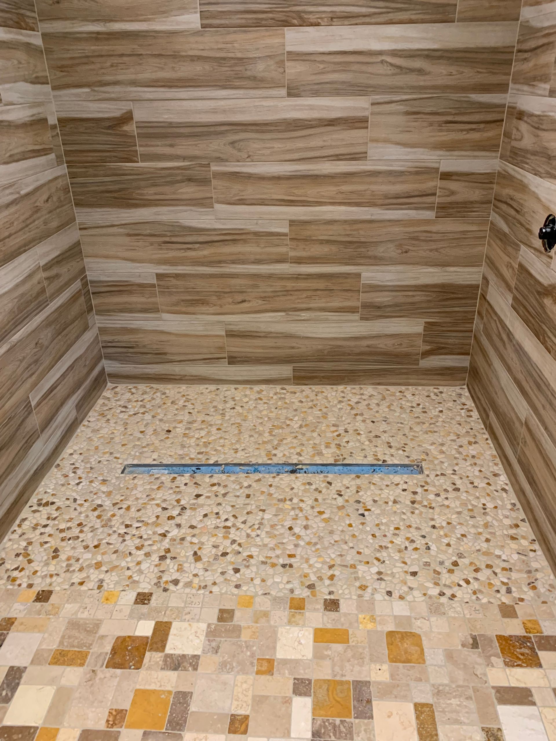 Shower interior with pebble floor, linear drain, and wood-look tile on walls.