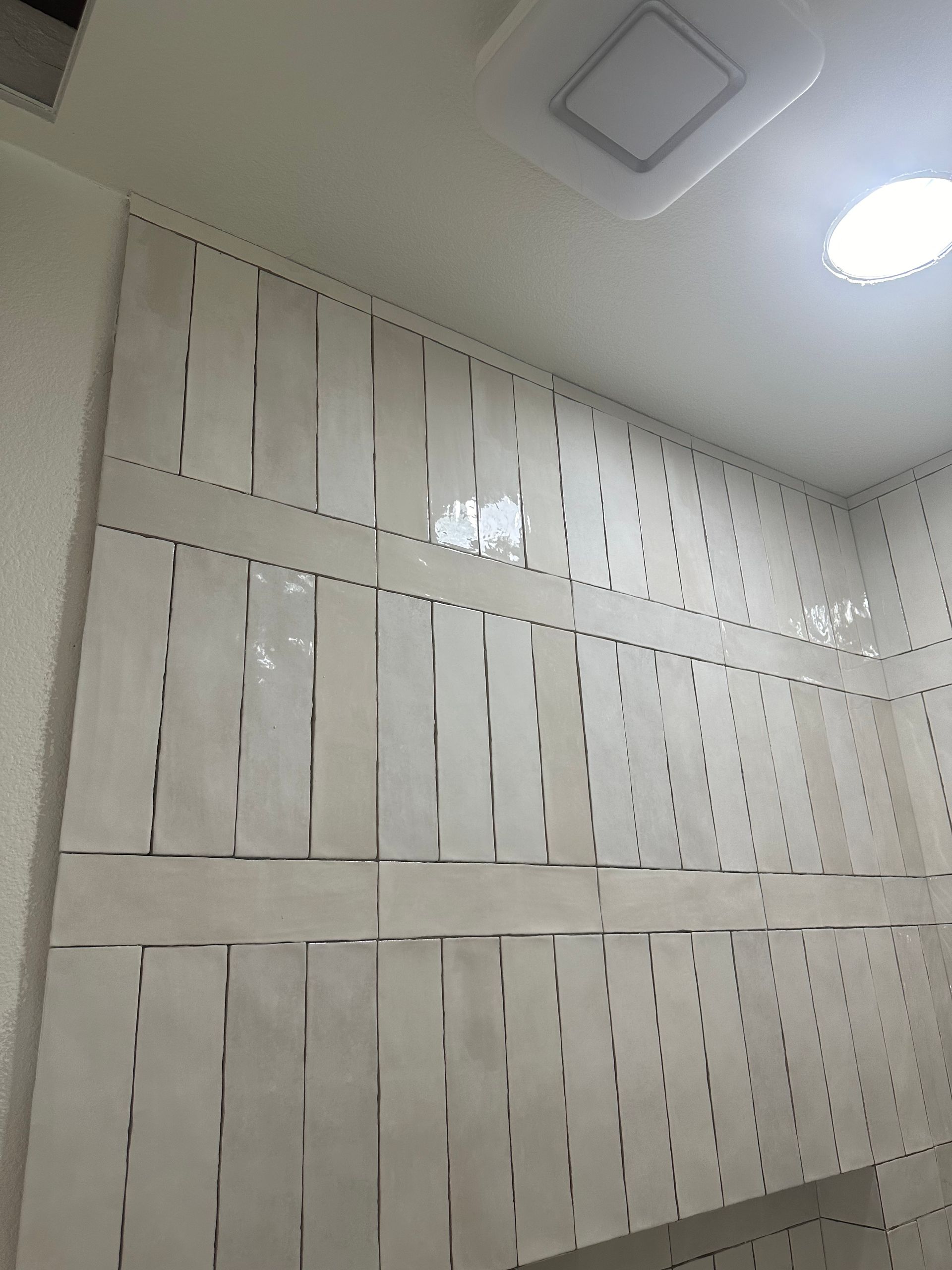 Tiled bathroom wall with ceramic white tile placed in a vertical and horizontal pattern.