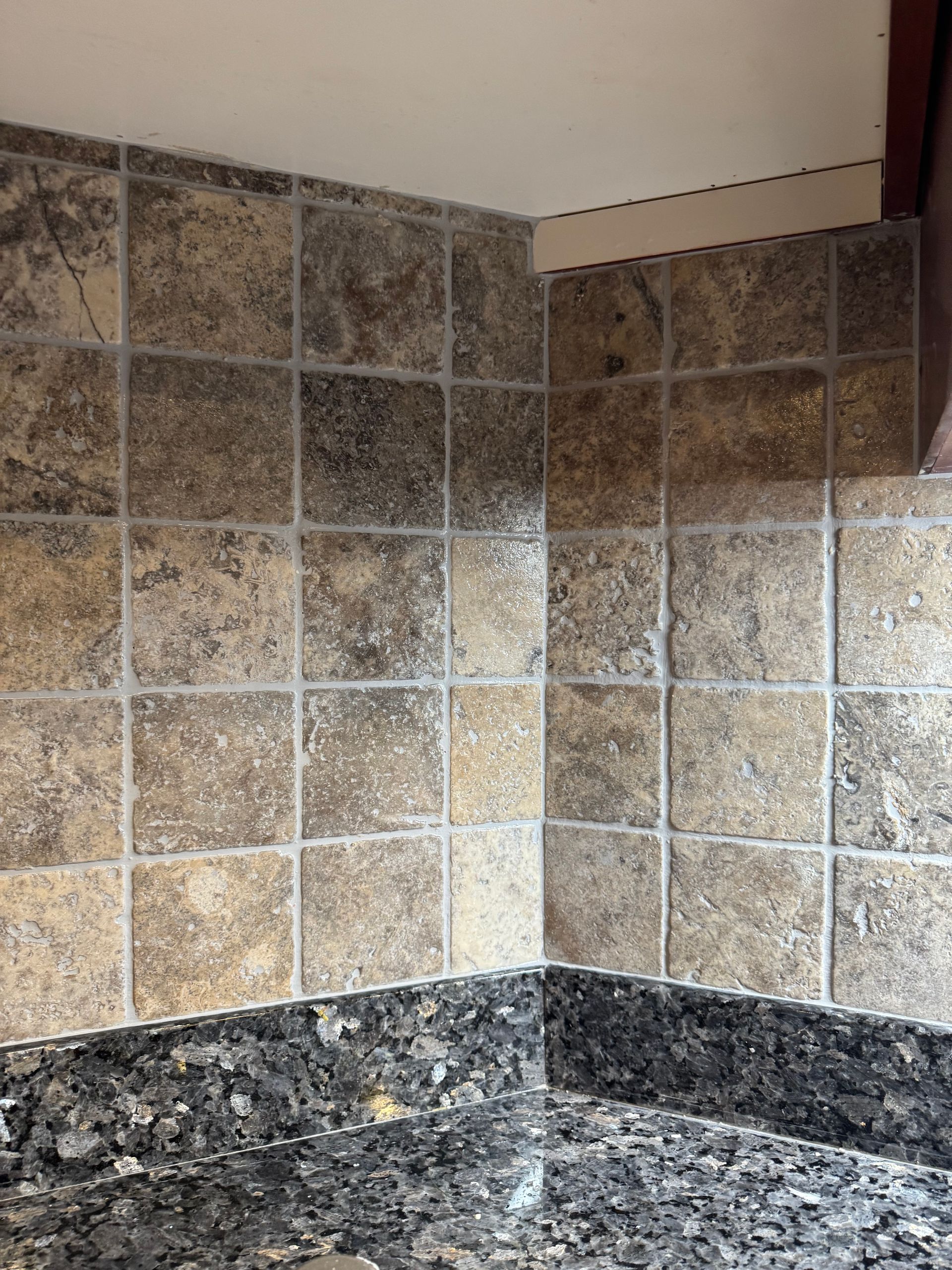 Corner of a kitchen featuring brown square tiles as a backsplash.