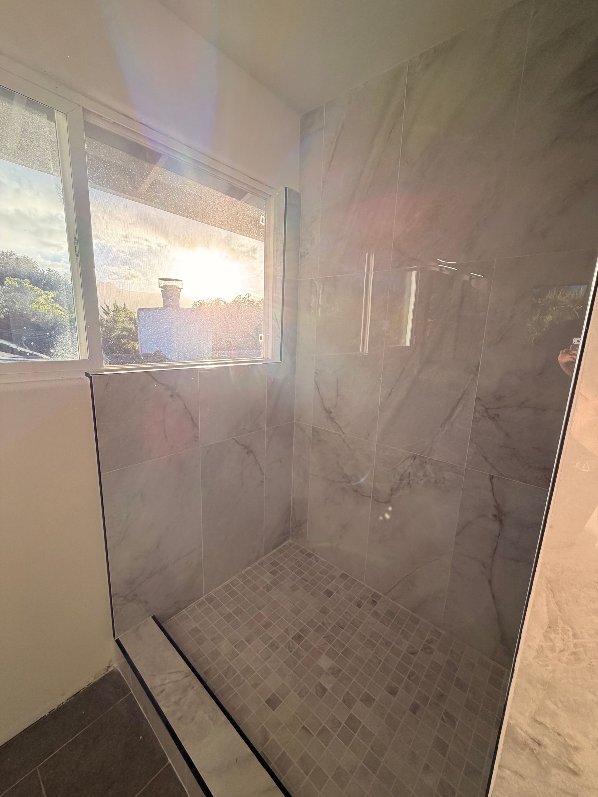 Marble like tile shower with a window. The floor and walls are stone. Sunlight streams in.