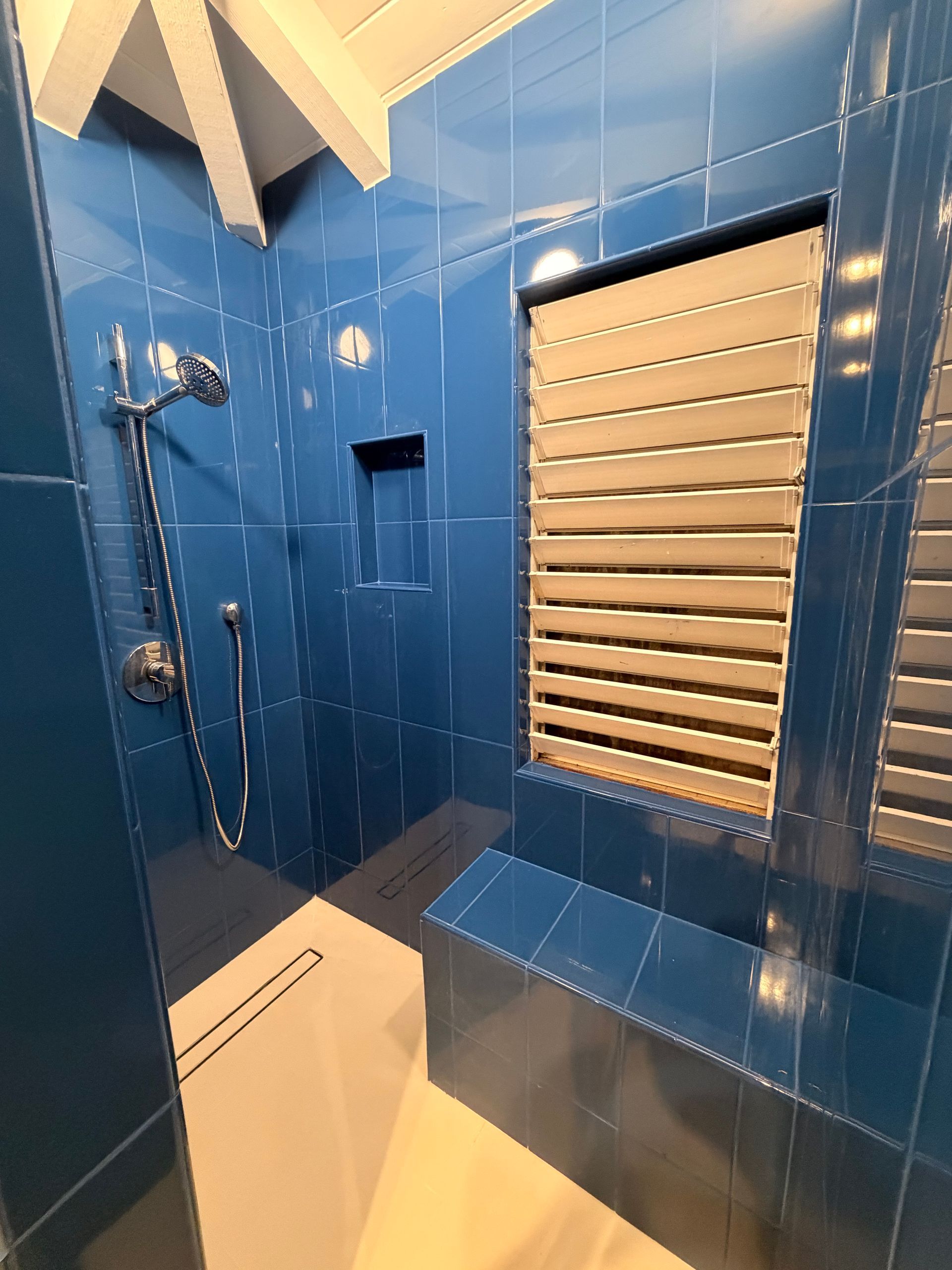 Blue tiled shower with rain showerhead, built-in storage, and horizontal slats.