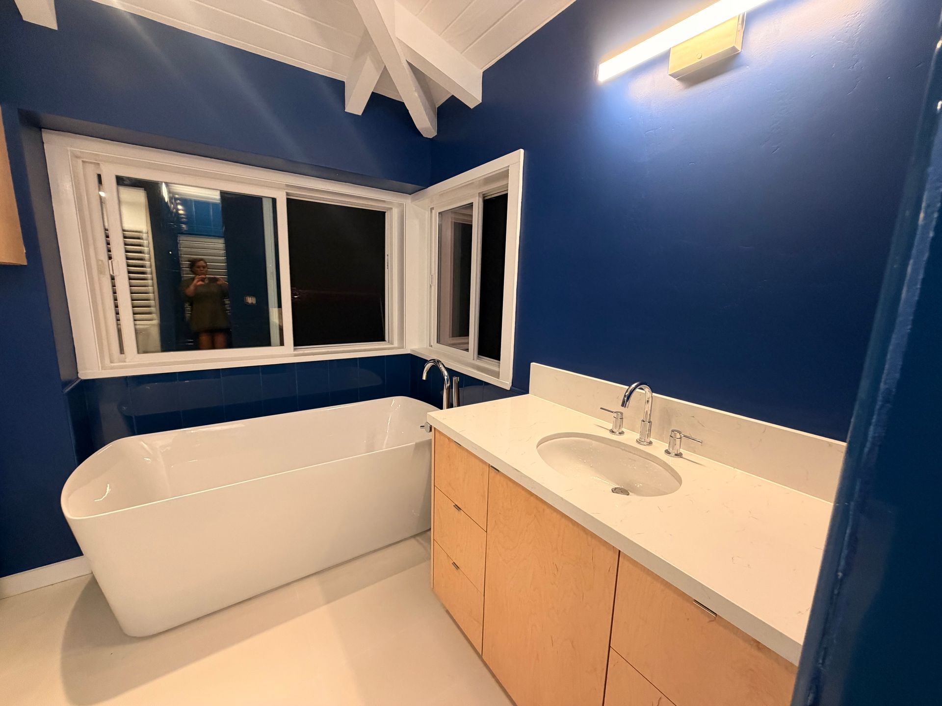 Blue bathroom with a white tub, sink, and wood vanity.