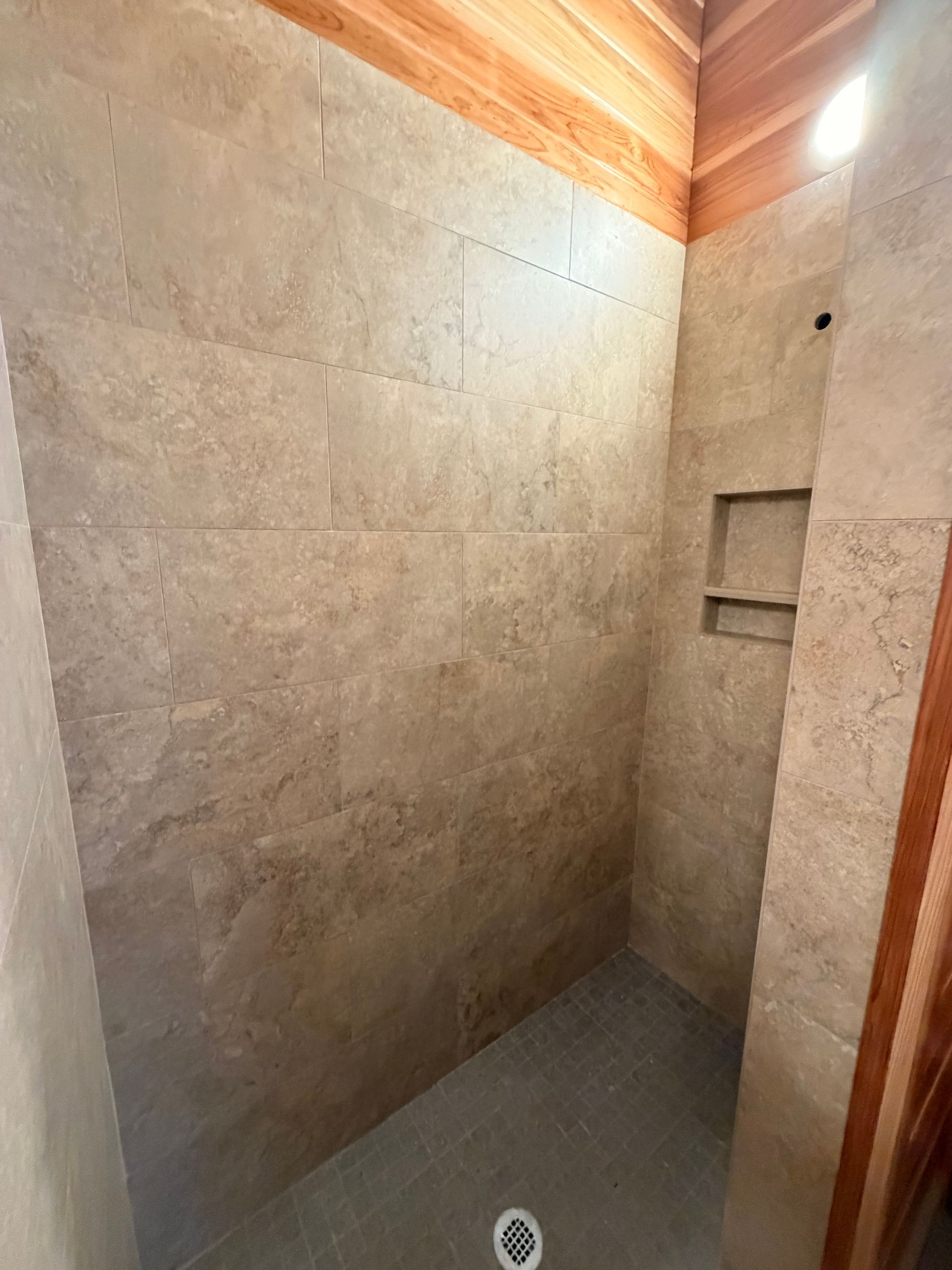 Stone-tiled shower with a gray floor drain and wooden ceiling accents