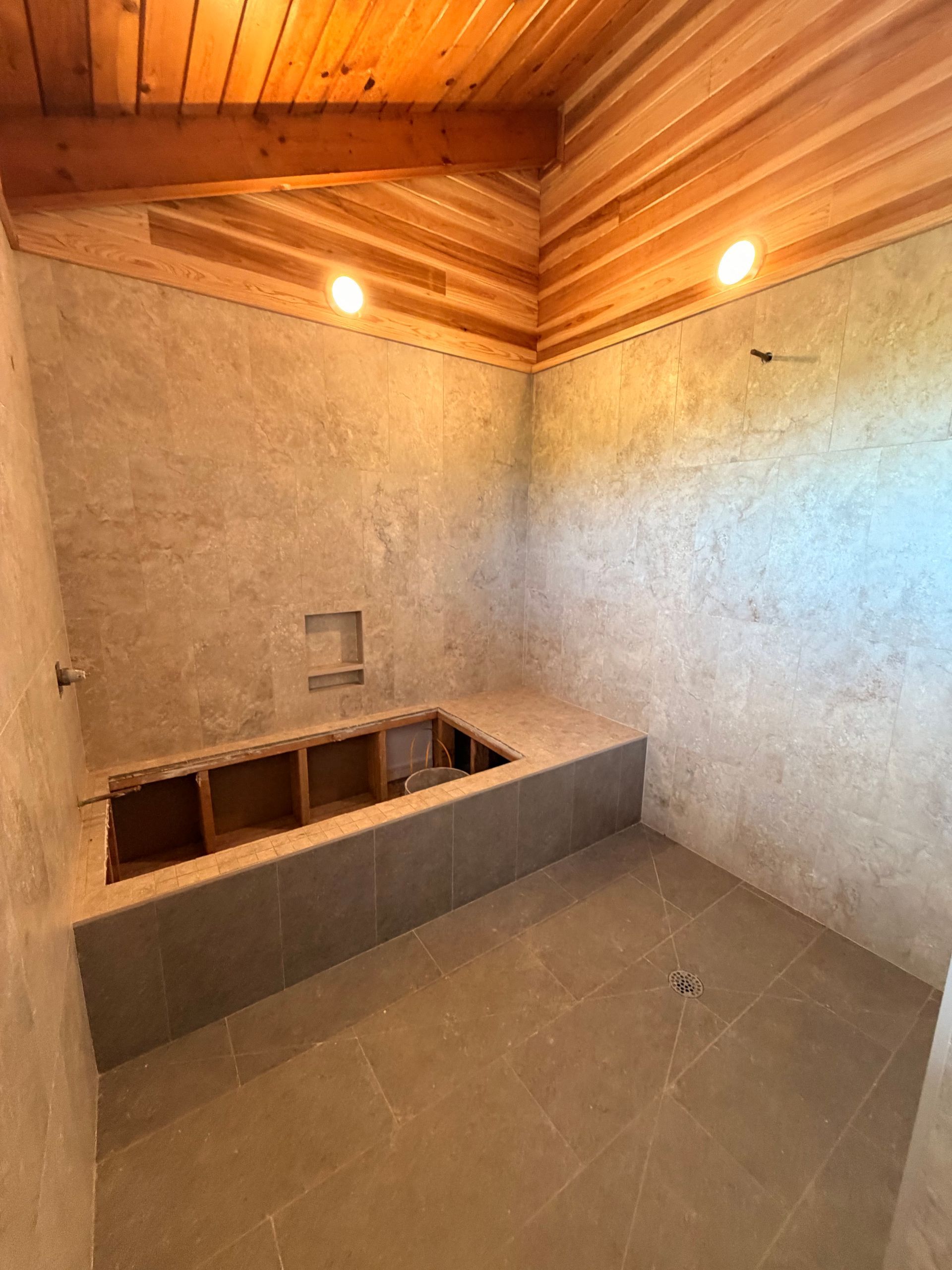 Small tiled bathroom under construction with a built-in bathtub and wood-paneled ceiling lights