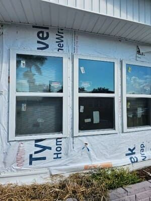 Partially finished house wall with three blue-framed windows and Tyvek house wrap exposed around them
