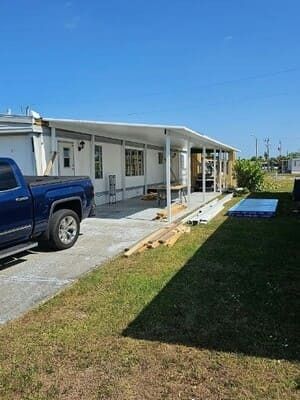 White mobile home with a blue pickup truck and a wheelchair ramp in a sunny yard