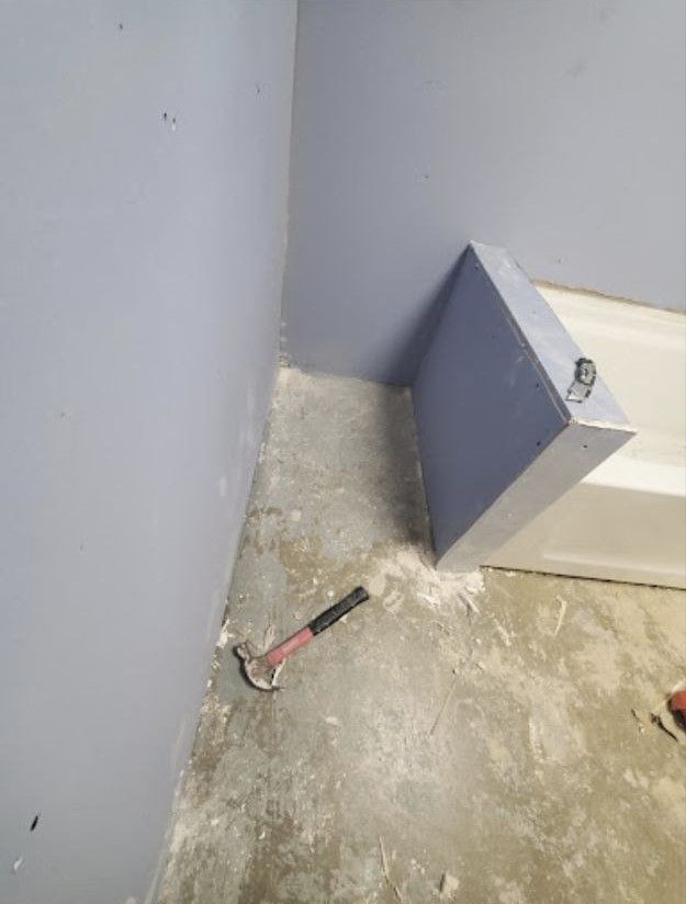A hammer is sitting on the floor in a bathroom next to a bathtub.