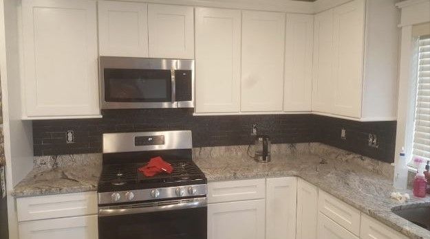 A kitchen with white cabinets , a stove , a microwave , and a sink.