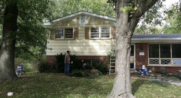 A man is standing in front of a house with a tree in front of it.