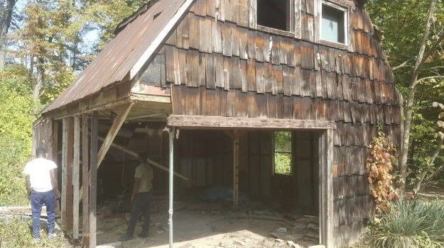 A man is standing in front of an old wooden barn.