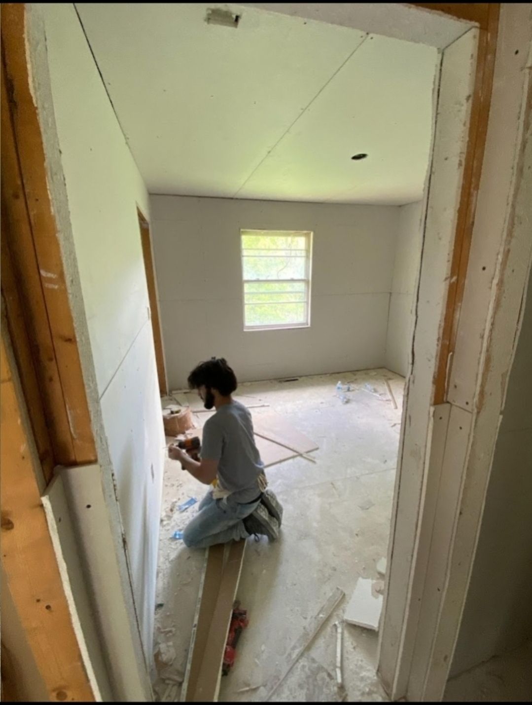 A man is kneeling down in a room while working on a wall.