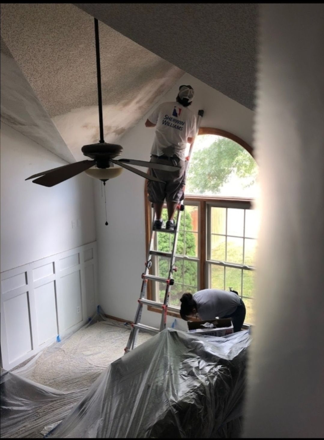 A man on a ladder paints the ceiling of a room