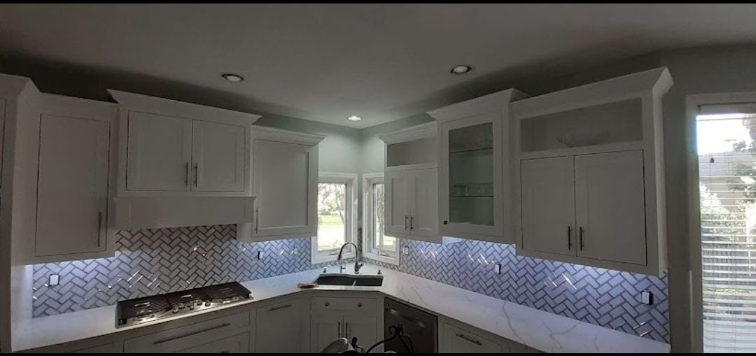 A kitchen with white cabinets , a stove , a sink , and a window.