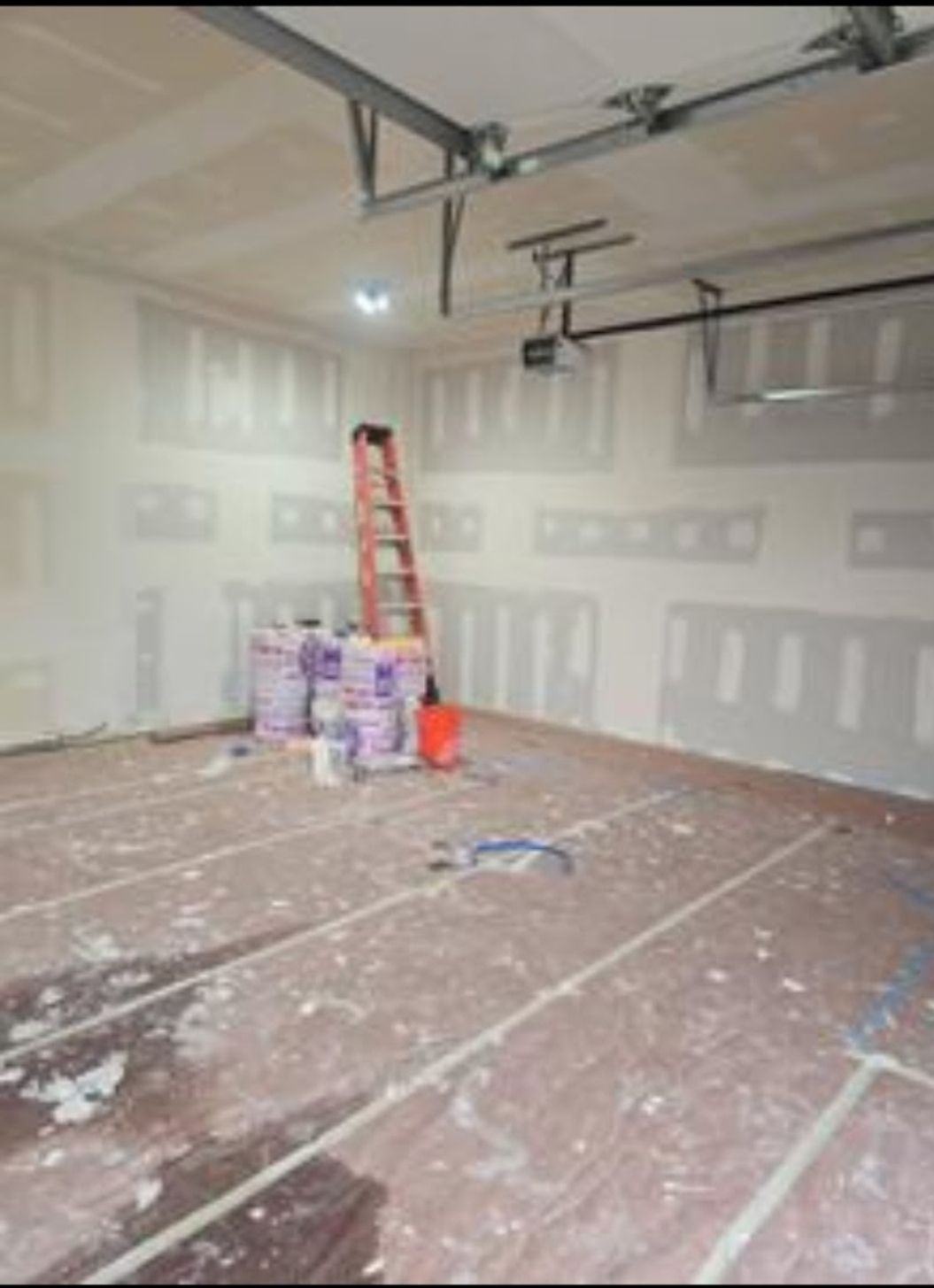 An empty garage with a ladder and buckets of paint.