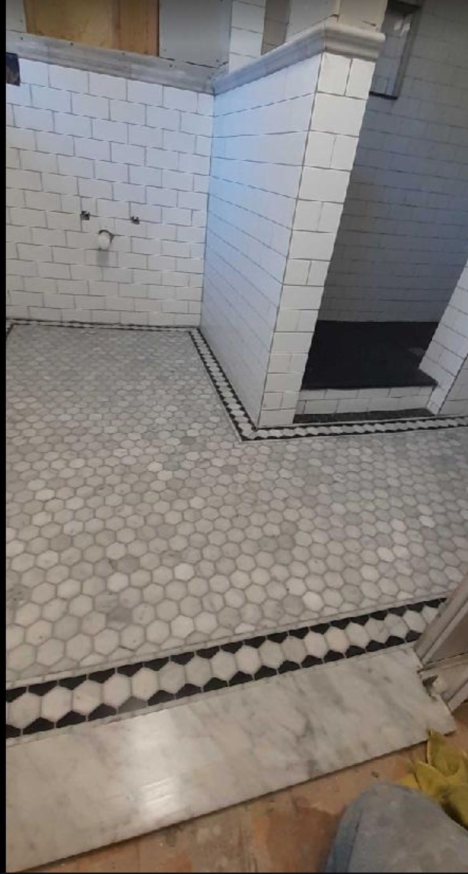A bathroom with white tiles and a black and white tile floor.
