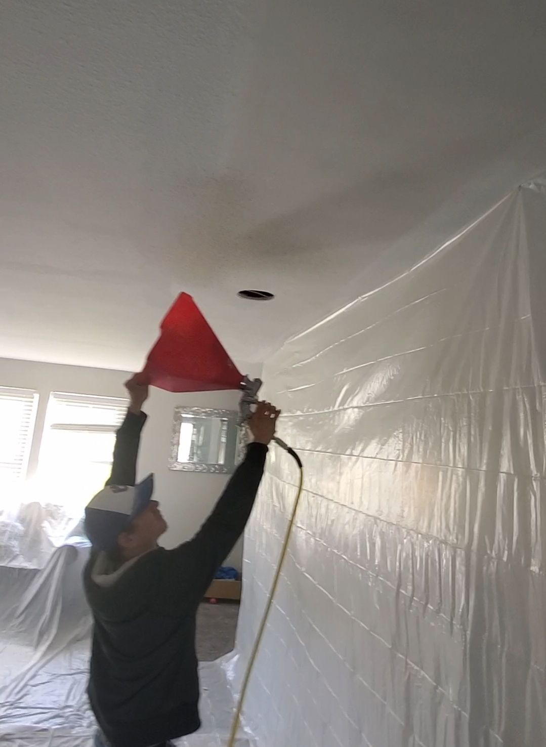 A man is spraying a ceiling with a red cone.